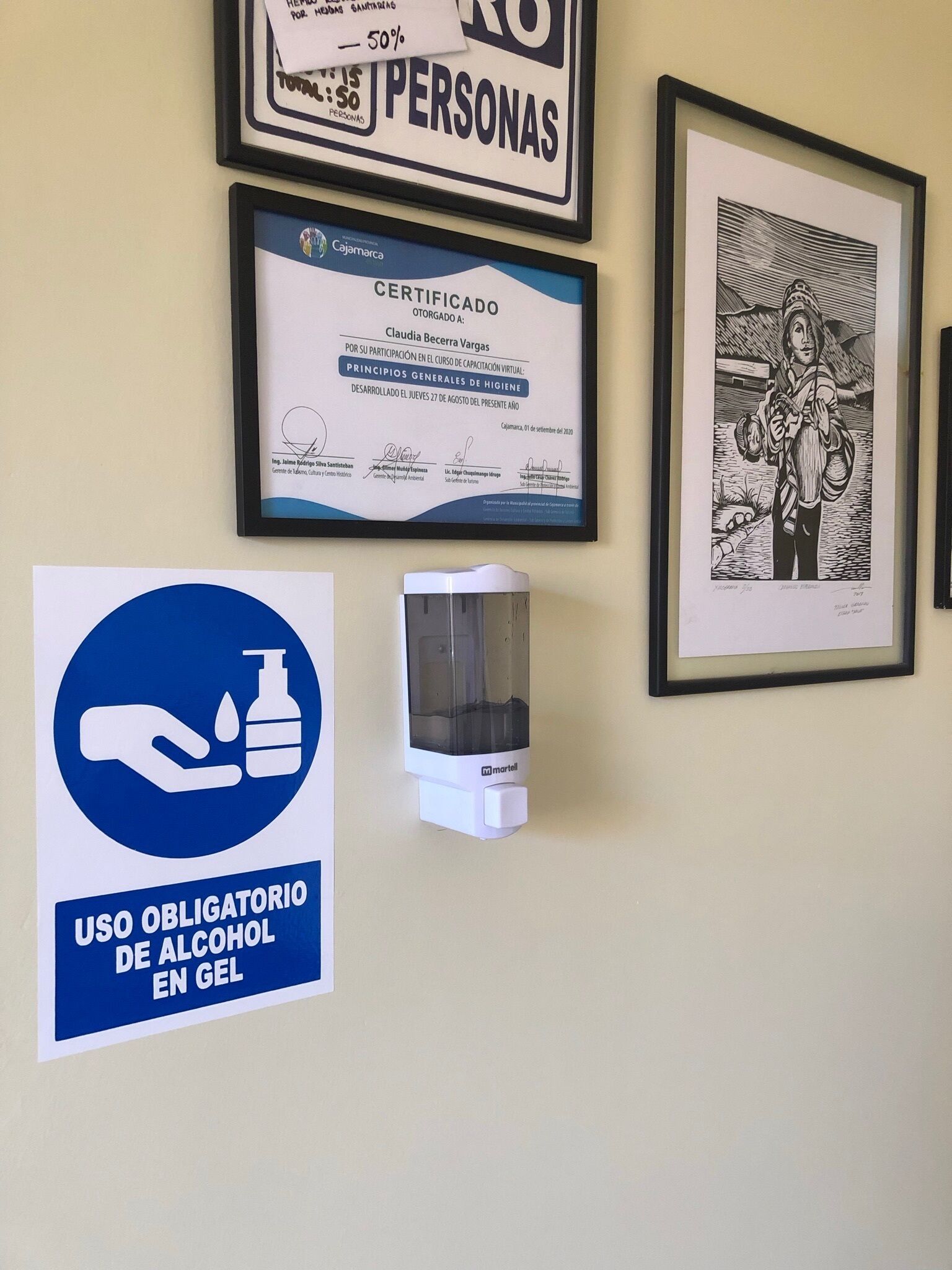 A wall with framed certificates, a framed artwork, and a hand sanitizer dispenser.