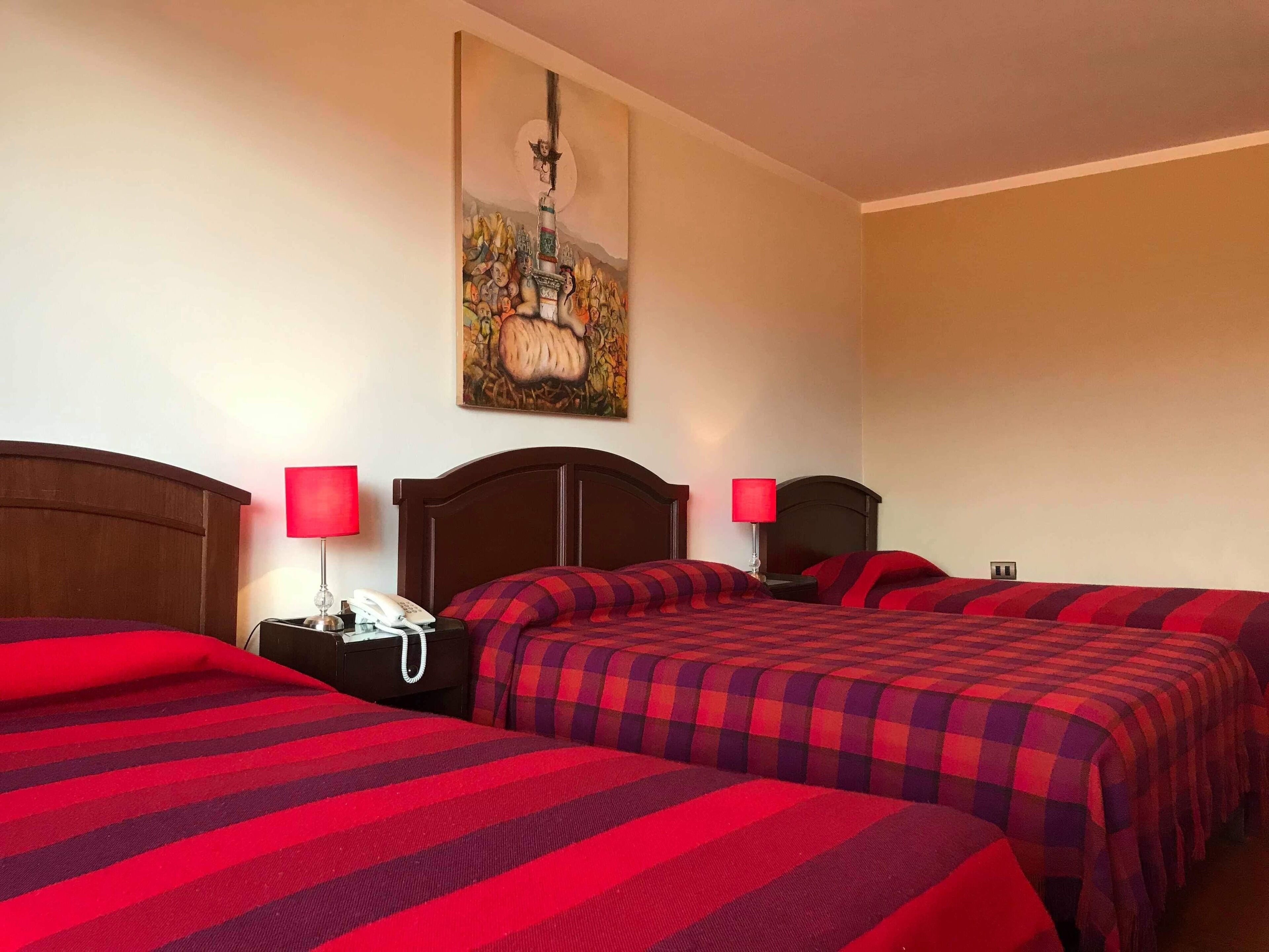 A hotel room with two beds, each with a red and black checkered bedspread, a wooden headboard, a nightstand with a lamp, and a painting on the wall.