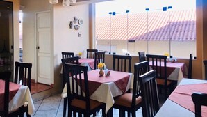 A dining area with multiple tables and chairs, a chandelier, and a view of a tiled roof through a window. - Valle del Inca (Cajamarca)