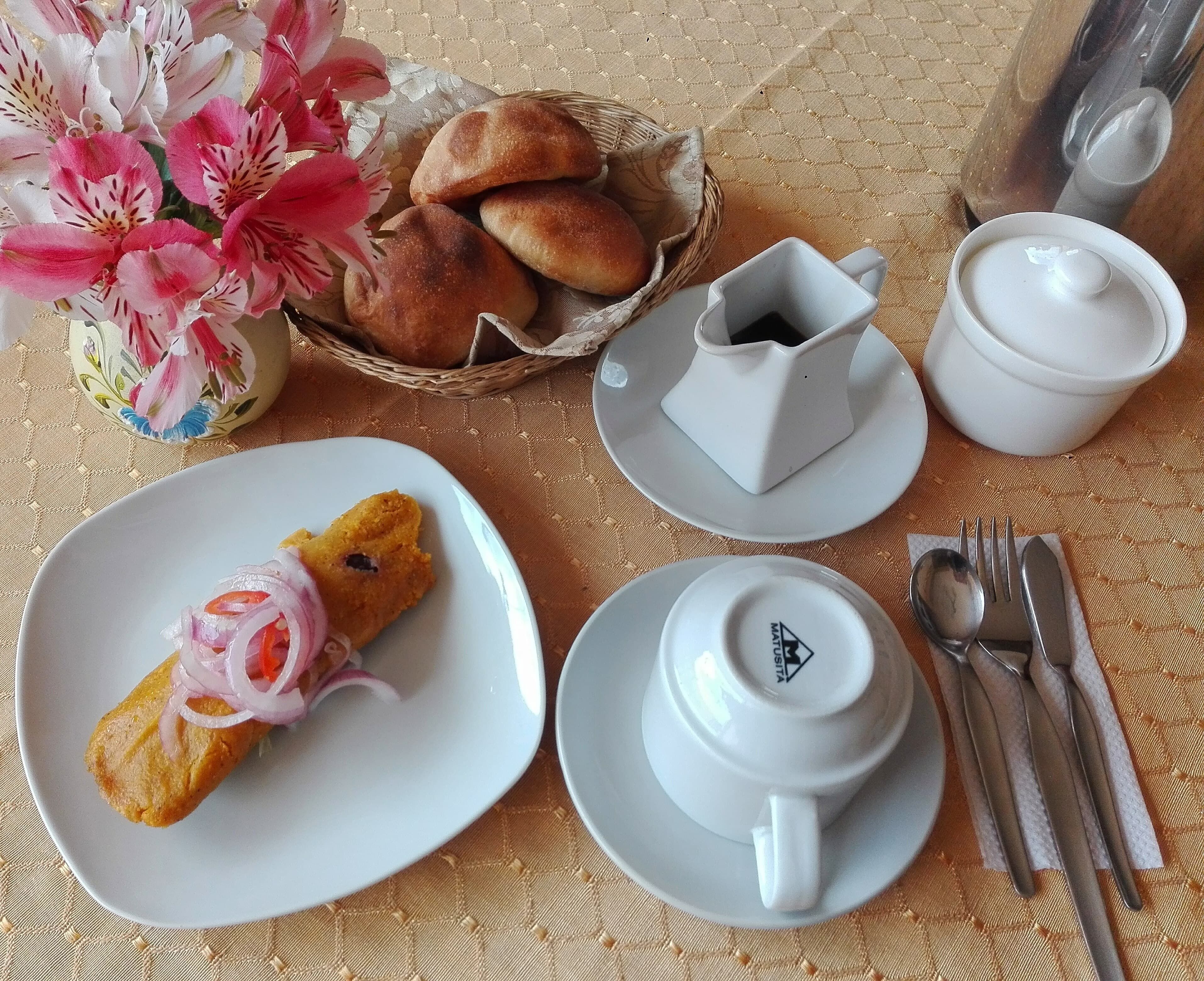 Une table dressée avec une assiette de nourriture, un panier de pain, une tasse, une soucoupe et des couverts.