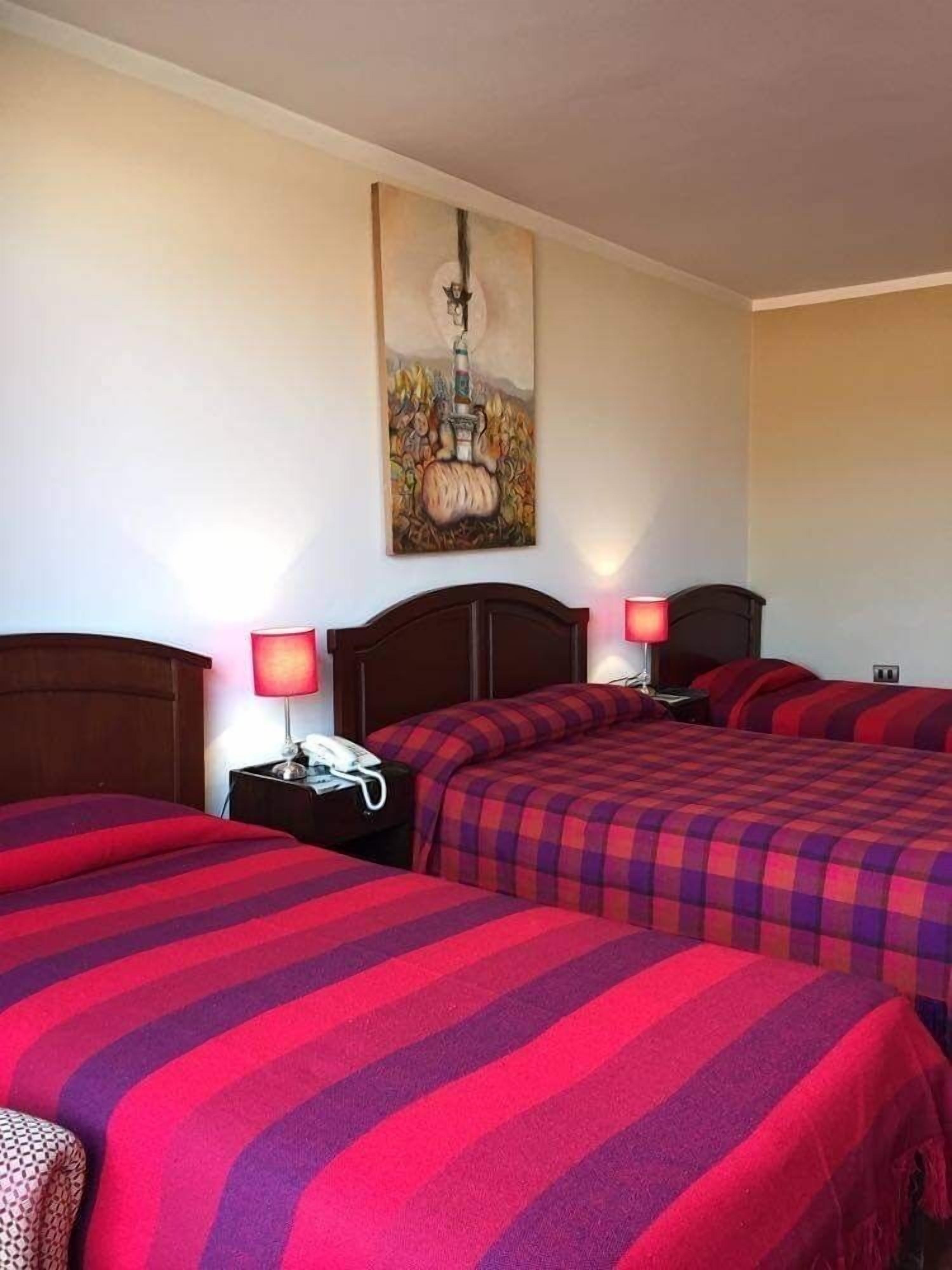 A hotel room with two beds, each with a red and purple striped bedspread, a wooden headboard, bedside lamps, and a painting on the wall.