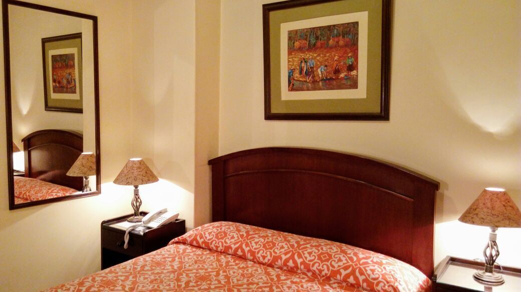 A hotel room with a large bed, two bedside tables, a nightstand, a mirror, and two framed pictures on the wall.