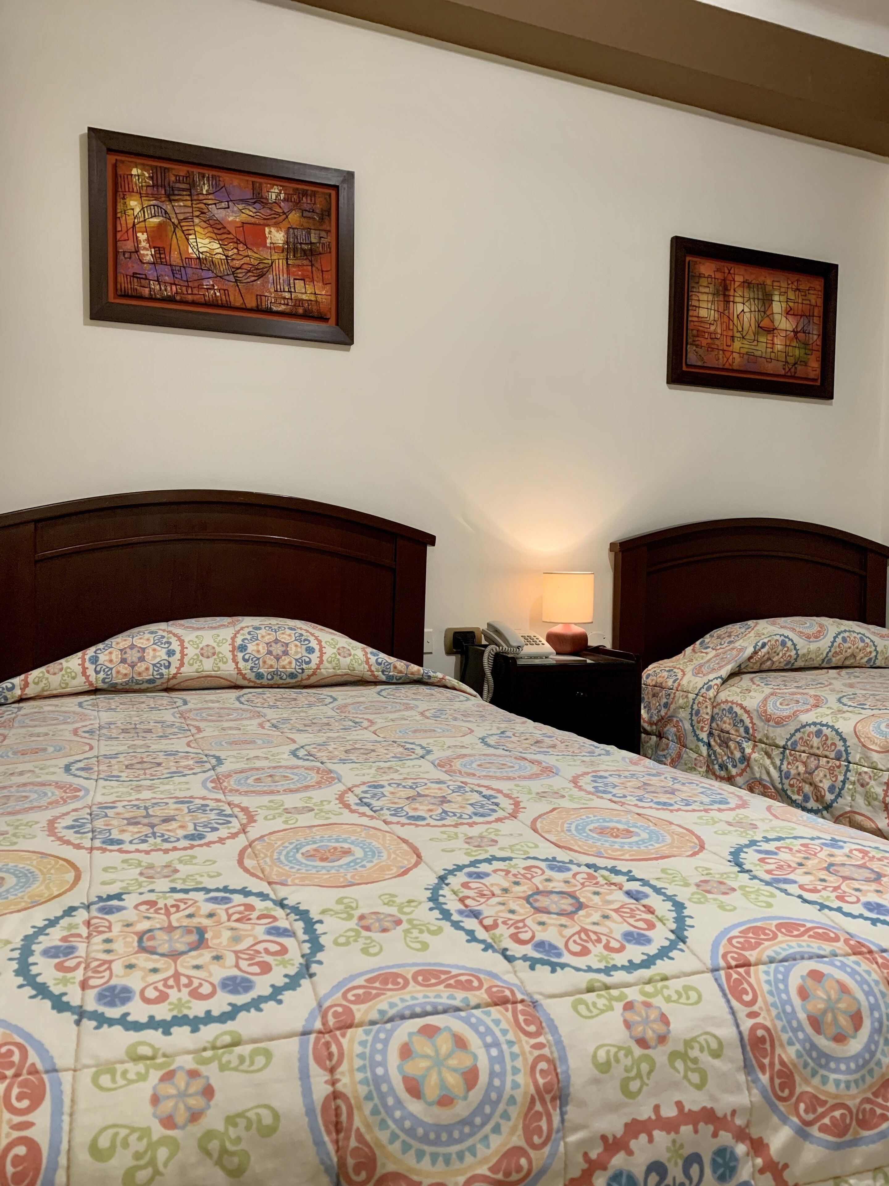 A hotel room with two beds, each with a patterned bedspread, a wooden headboard, and a nightstand with a lamp.