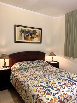 A hotel room with a bed, two bedside tables, a lamp on each table, a framed abstract painting on the wall, and a window with curtains. - Valle del Inca (Cajamarca)