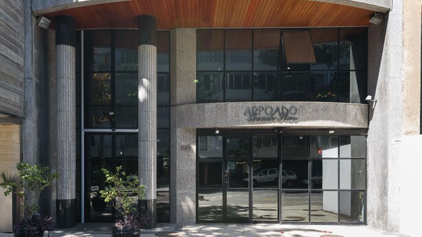 A modern building entrance with a curved wooden ceiling, large glass doors, and potted plants. - Omar do Rio - Apartamento FO407 (Rio de Janeiro)