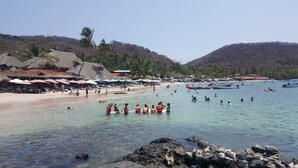 Platja amb aigua cristal·lina, ombrel·les i persones nedant.