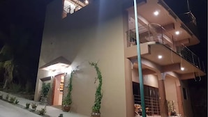 Un edifici de diverses plantes amb un balcó al pis superior, plantes en testos i una escala que condueix a l'entrada.