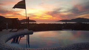 Una piscina amb vistes a un capvespre sobre un paisatge costaner, una bandera i una cadira de relax.