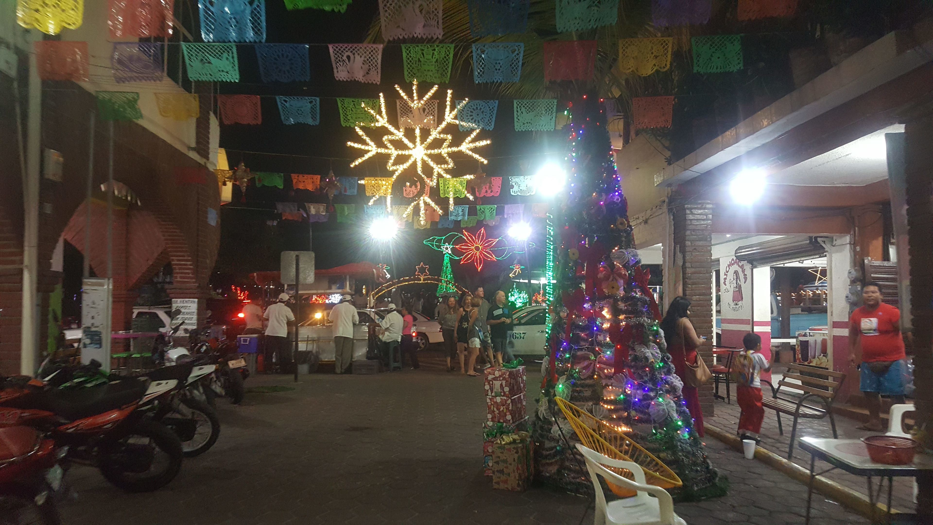 Un mercado navideño con un árbol de Navidad decorado, coloridas adornos colgantes y fachada de un edificio de ladrillo.