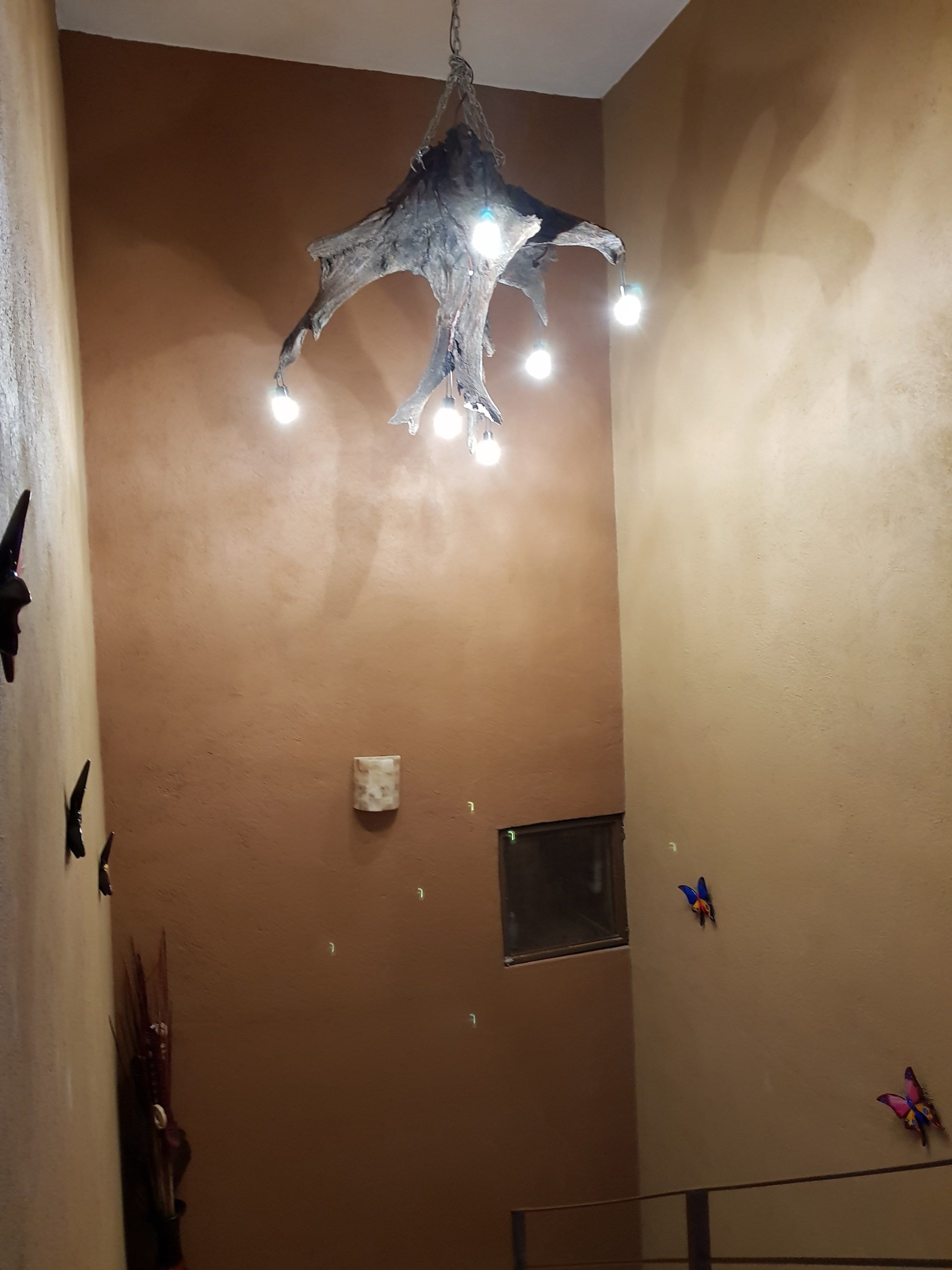 Una habitación con una lámpara colgante de madera original, un ventanal pequeño y adornos de pared con mariposas.