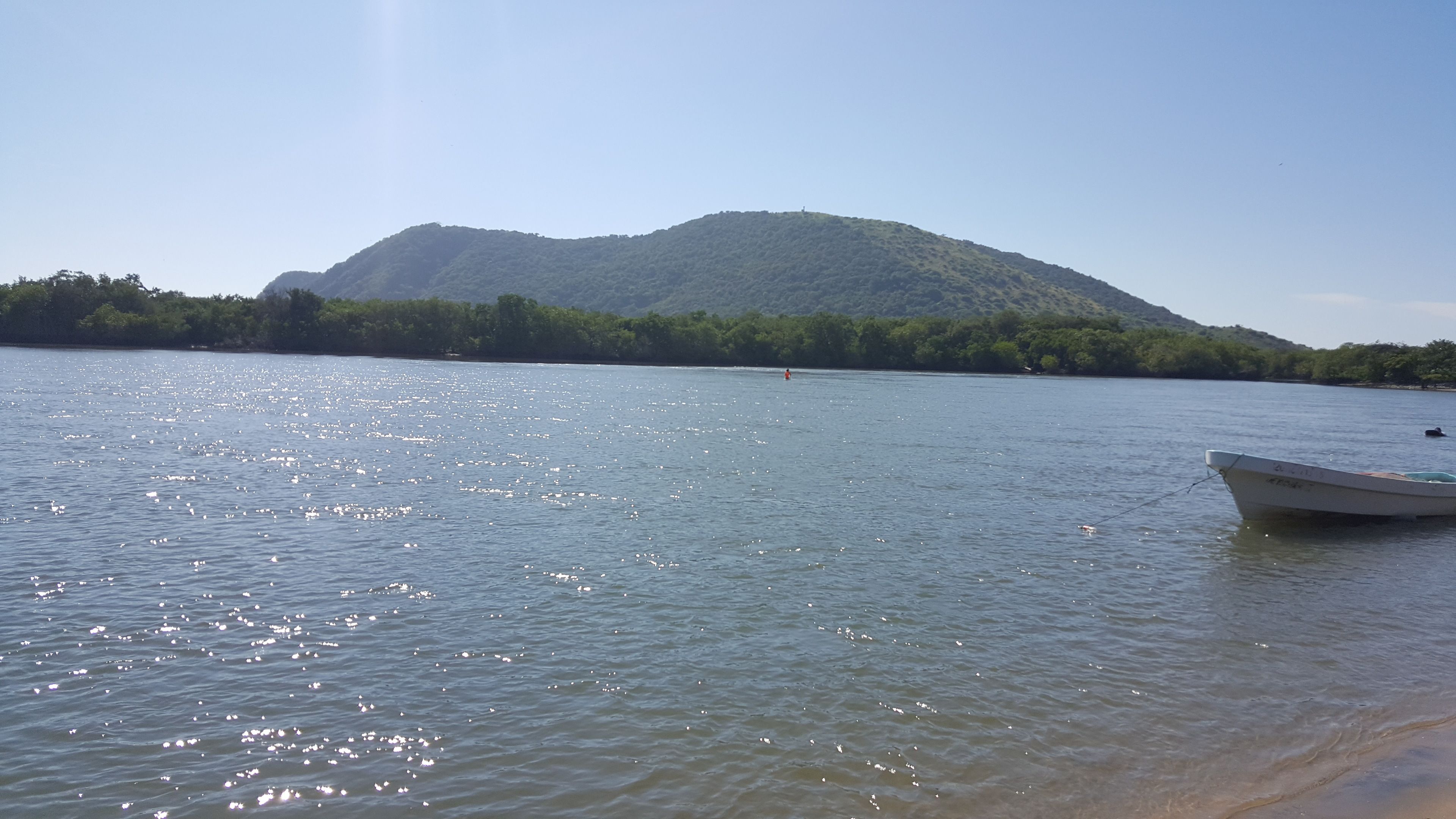 Un lago tranquilo con un bote amarrado a la derecha, rodeado por una ladera boscosa.