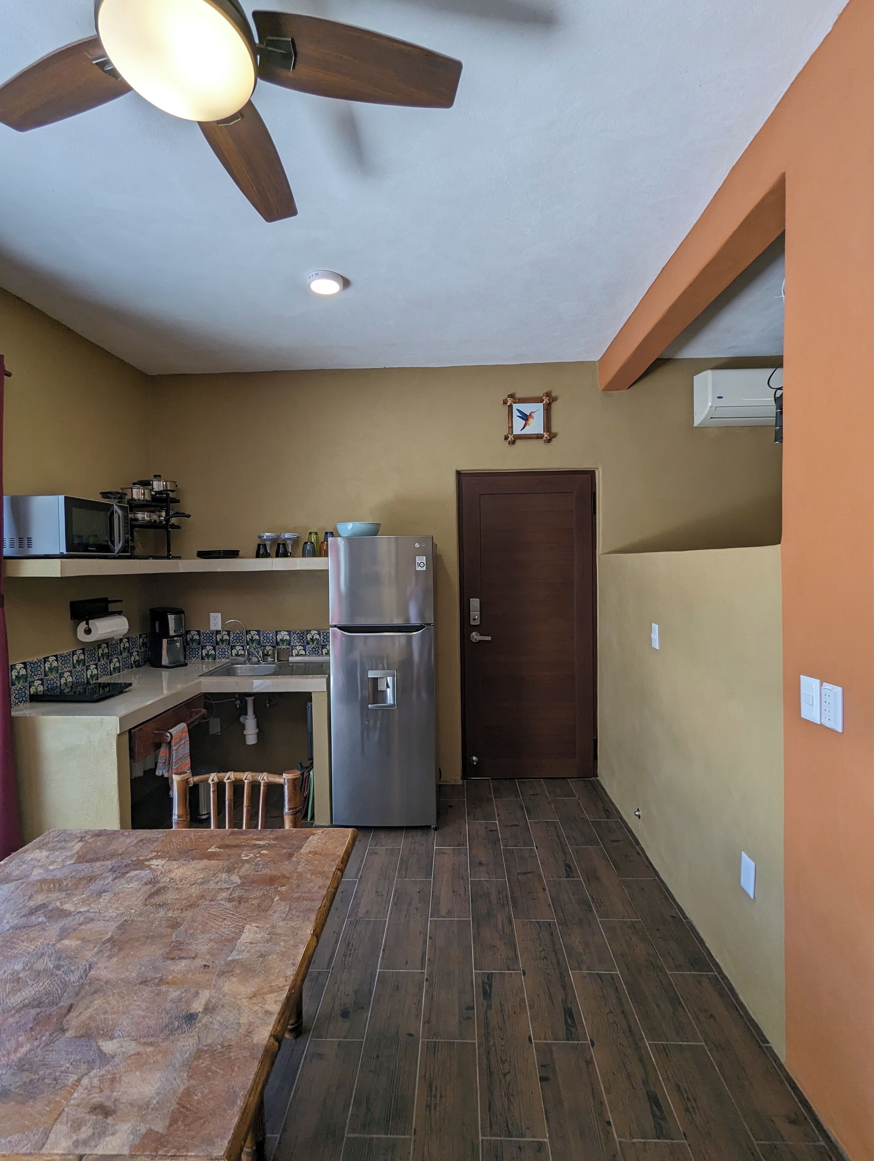 Una cocina compacta con ventilador de techo de madera, un refrigerador, un microondas y un lavamanos.