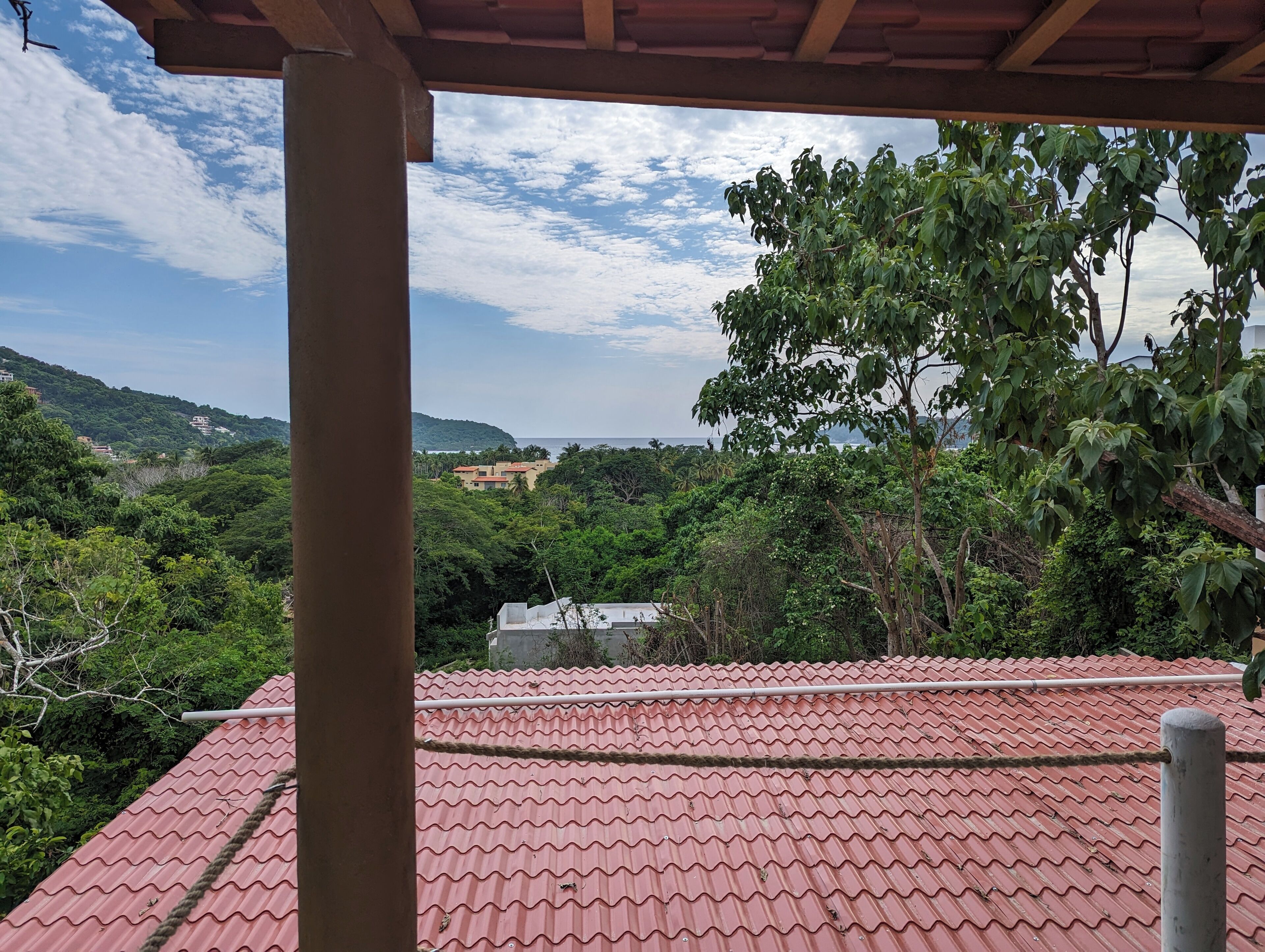 A red-tiled roof, a view of a lush green landscape, and a clear sky.