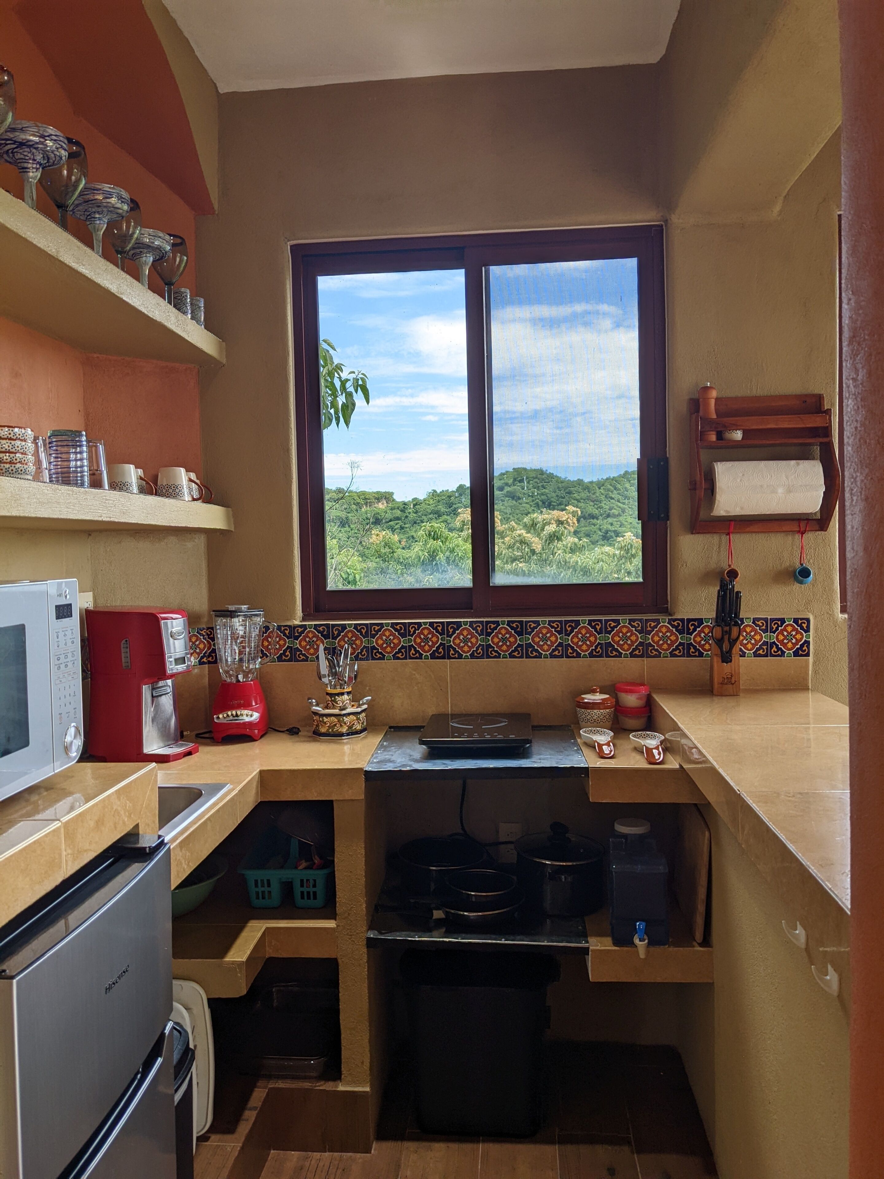 A compact kitchen with a window view, a microwave, a red coffee maker, and a blender.
