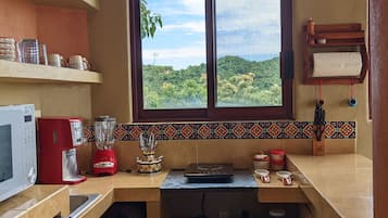 A compact kitchen with a window view, a microwave, a red coffee maker, and a blender.