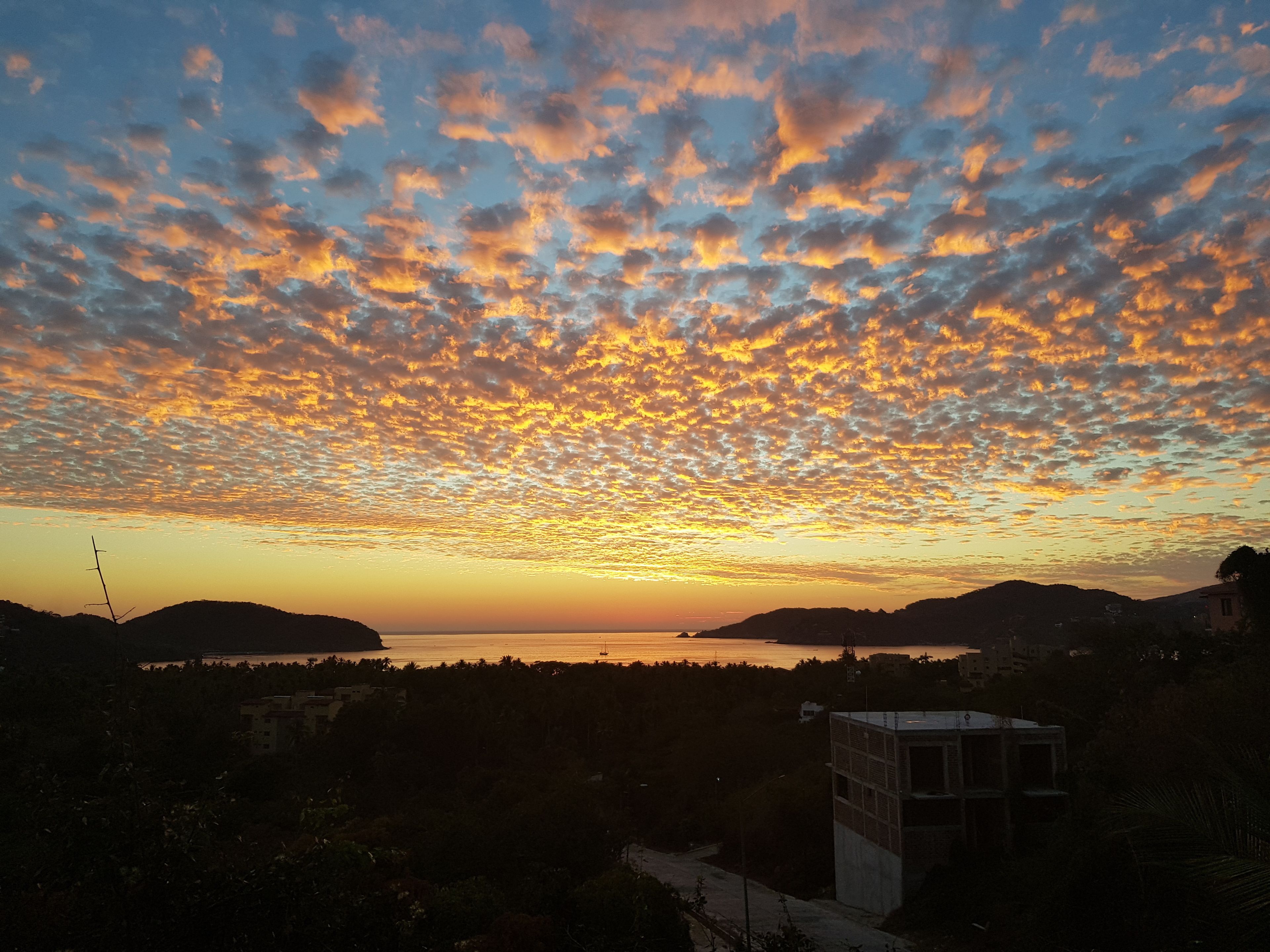 A sunset over a body of water with a silhouette of hills and a small building in the foreground.