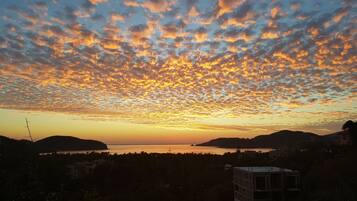 A sunset over a body of water with a silhouette of hills and a small building in the foreground.