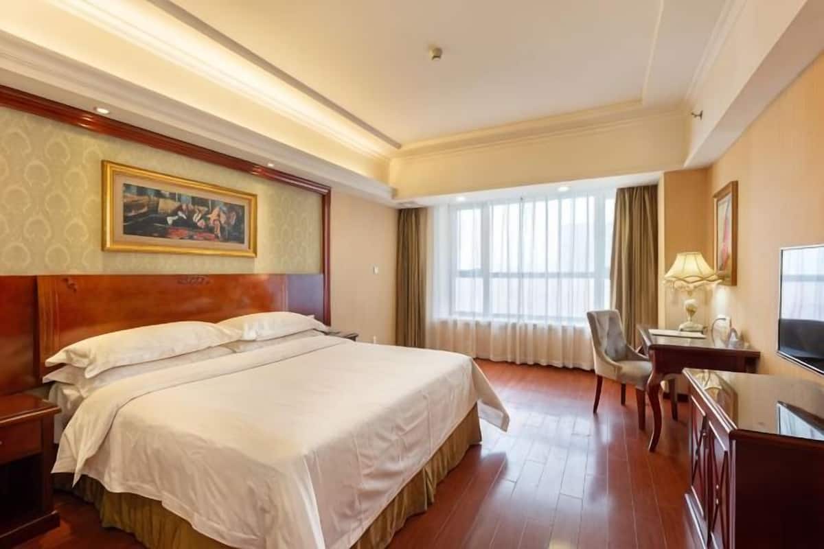 Une chambre d’hôtel avec un grand lit, un bureau avec une chaise, une télévision et une fenêtre avec des rideaux.