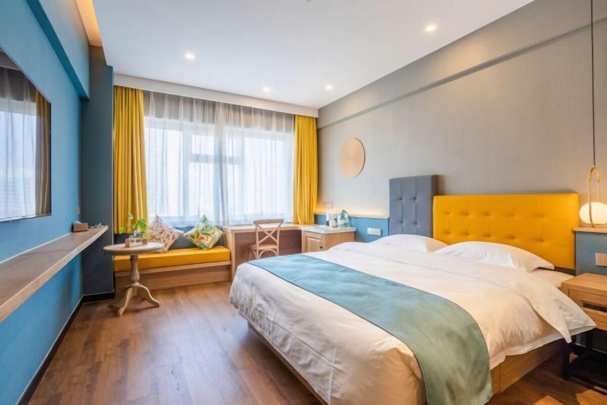 Ett hotellrum med en säng, ett skrivbord, en stol och ett fönster med gardiner.