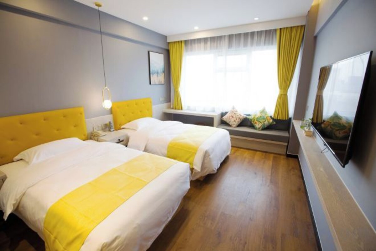 Una camera d'albergo con due letti, un'ampia finestra con tende, una TV a schermo piatto e un comodino.