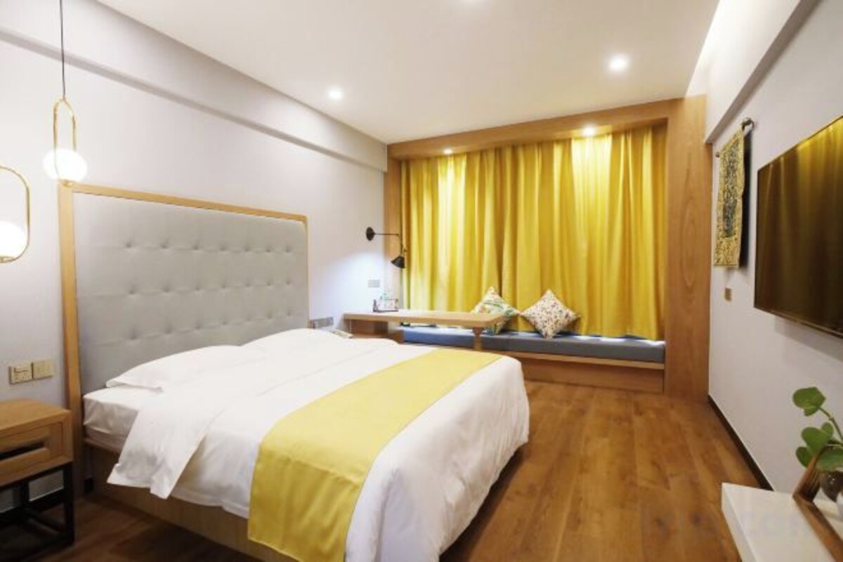 Una camera d'albergo con un letto grande, un comodino, una scrivania, una finestra con tende e una pianta.