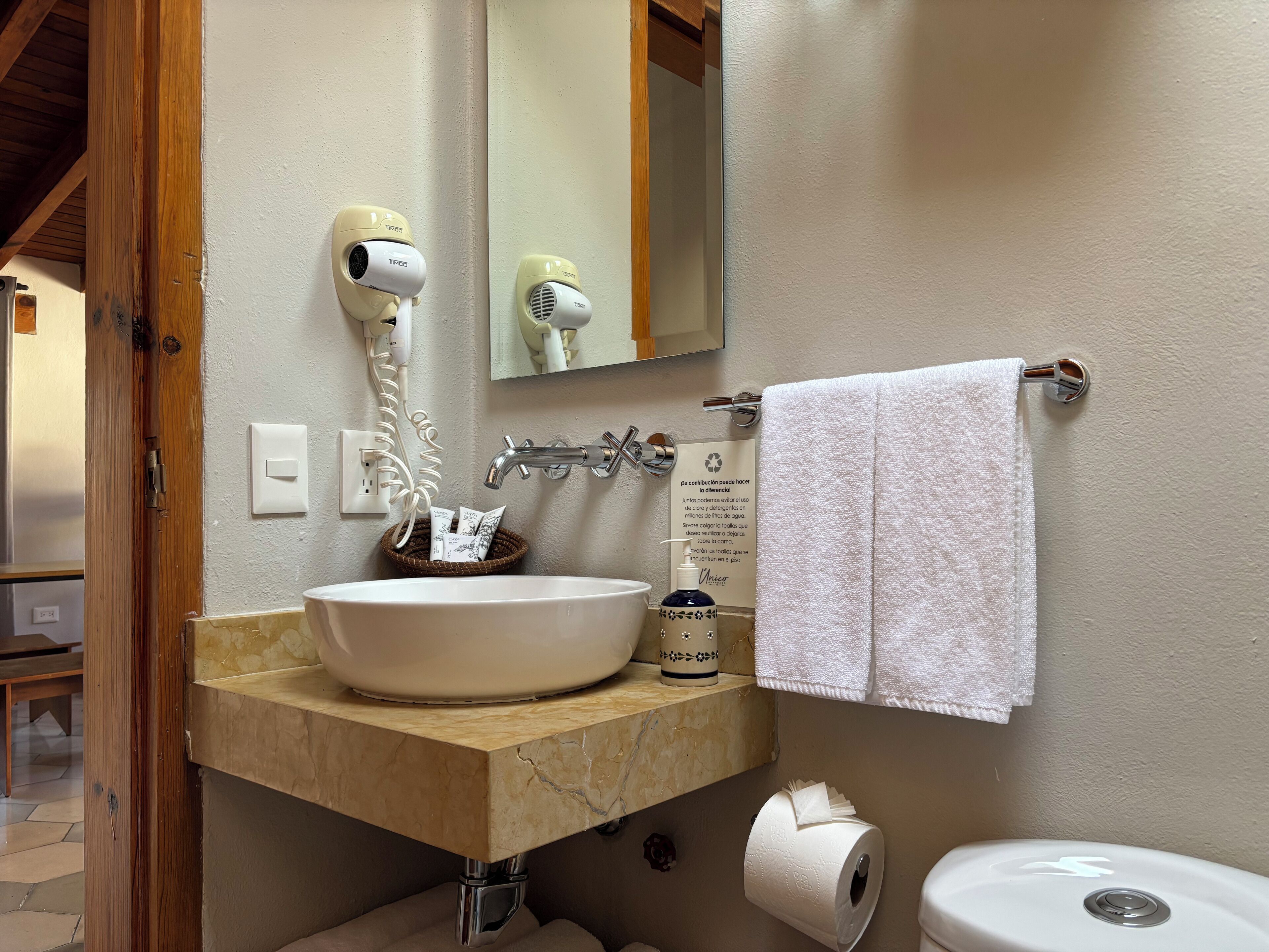 Une salle de bain équipée d’un lavabo en marbre, d’un sèche-cheveux, d’un porte-serviettes, d’un rouleau de papier toilette et d’un miroir.