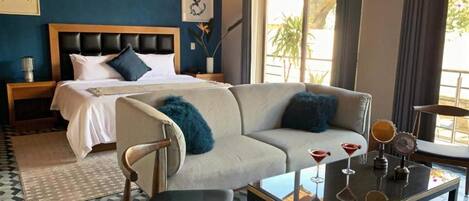 Une chambre d’hôtel avec un lit, un canapé, une table basse avec des boissons, et une vue sur l’extérieur.