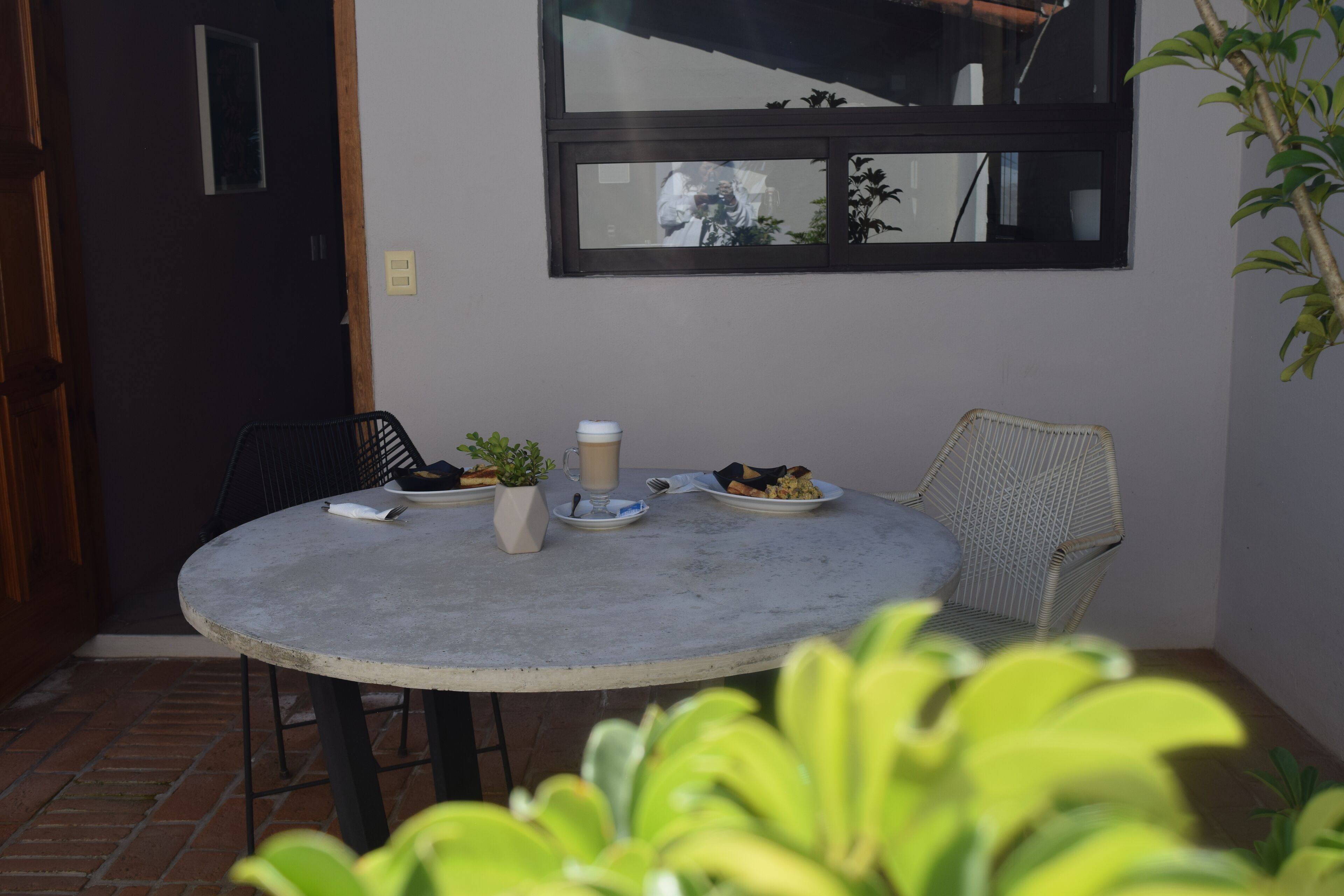 Una mesa redonda con una taza de café, platos de comida y una pequeña planta en maceta.