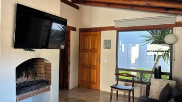 Una sala de estar con chimenea, televisor montado encima y una puerta de madera, con ventana que ofrece vistas a la vegetación.