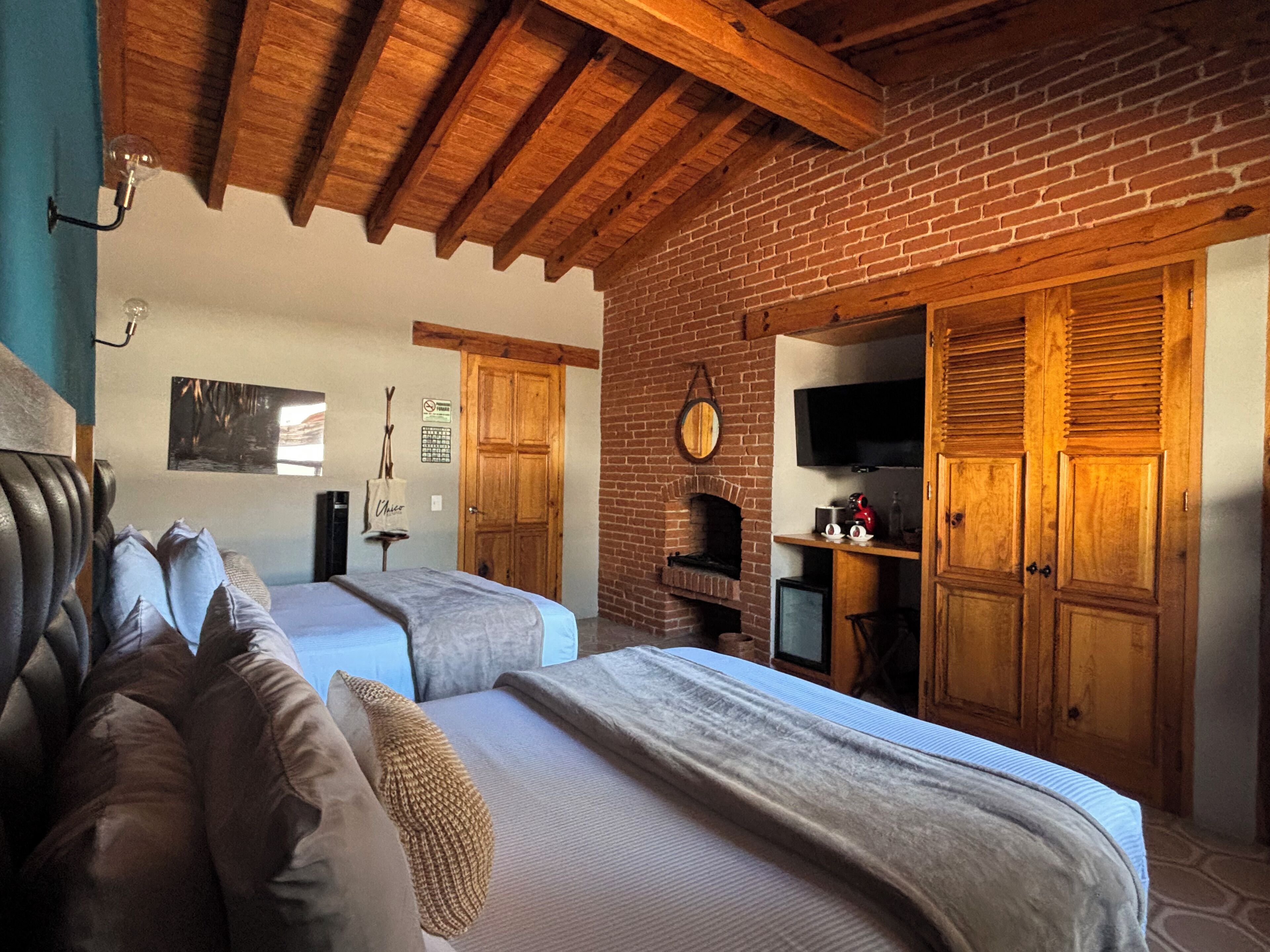 A bedroom with a brick fireplace, wooden ceiling beams, and a television mounted on the wall.