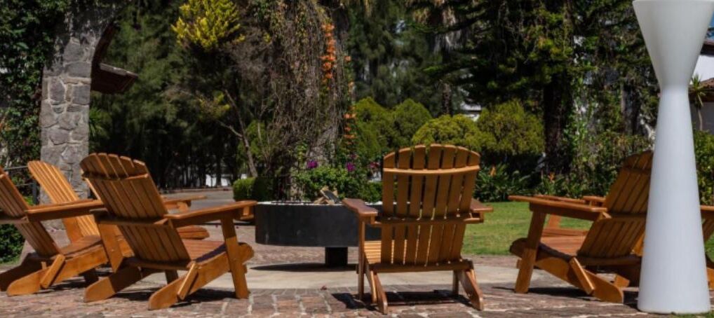 Un patio con sillas Adirondack de madera dispuestas alrededor de una mesa central, con árboles y un muro de piedra de fondo.