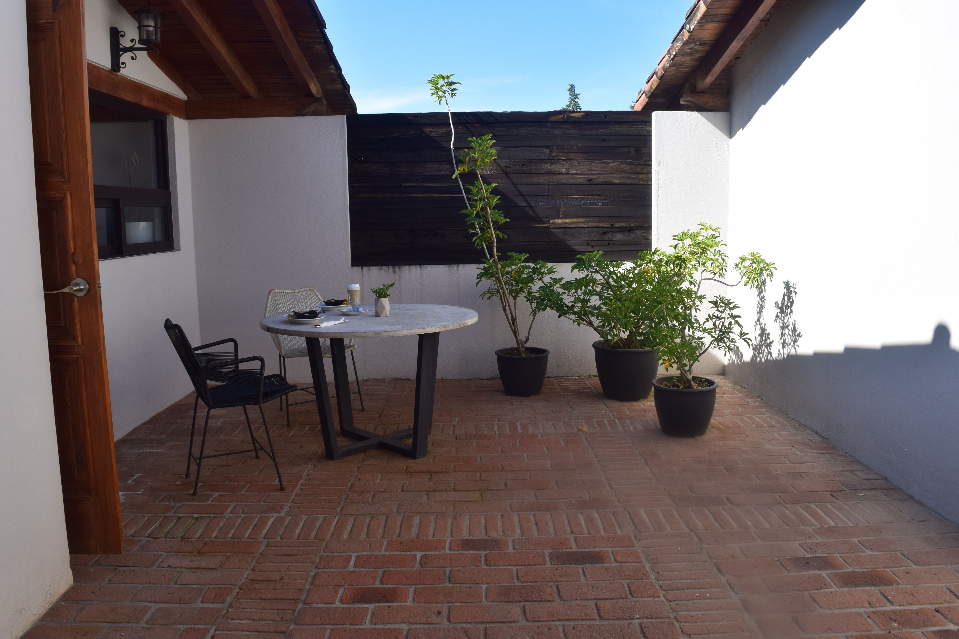 A patio with a round table and chairs, potted plants, and a wooden ceiling.