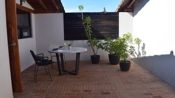 A patio with a round table and chairs, potted plants, and a wooden ceiling.
