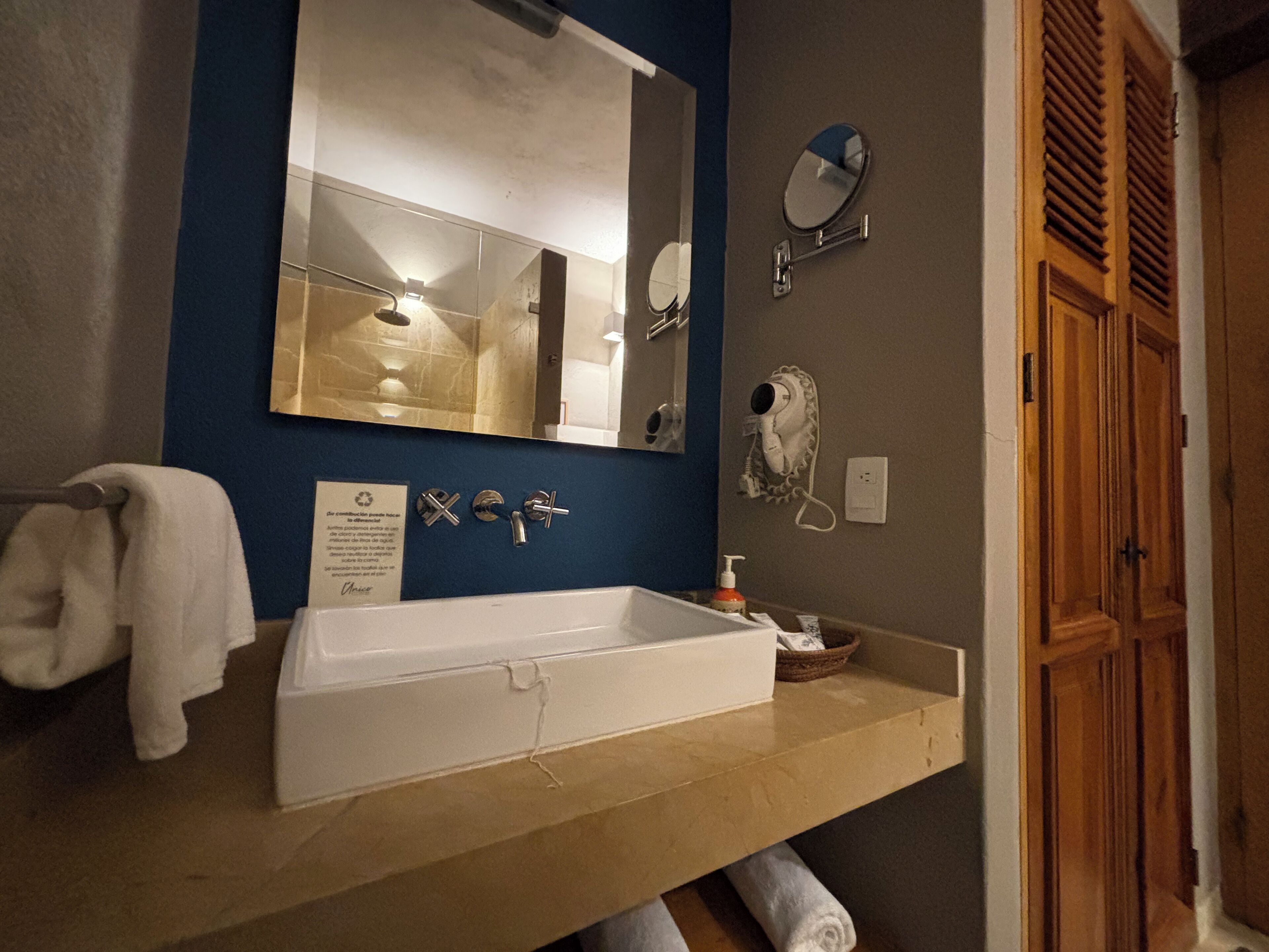 A bathroom with a large mirror, a sink, and a hairdryer mounted on the wall.