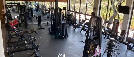 A gym with various exercise equipment, large windows, and a wooden ceiling.