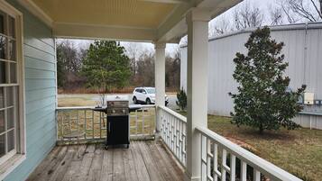 A covered porch with a grill, a white fence, and a tree.