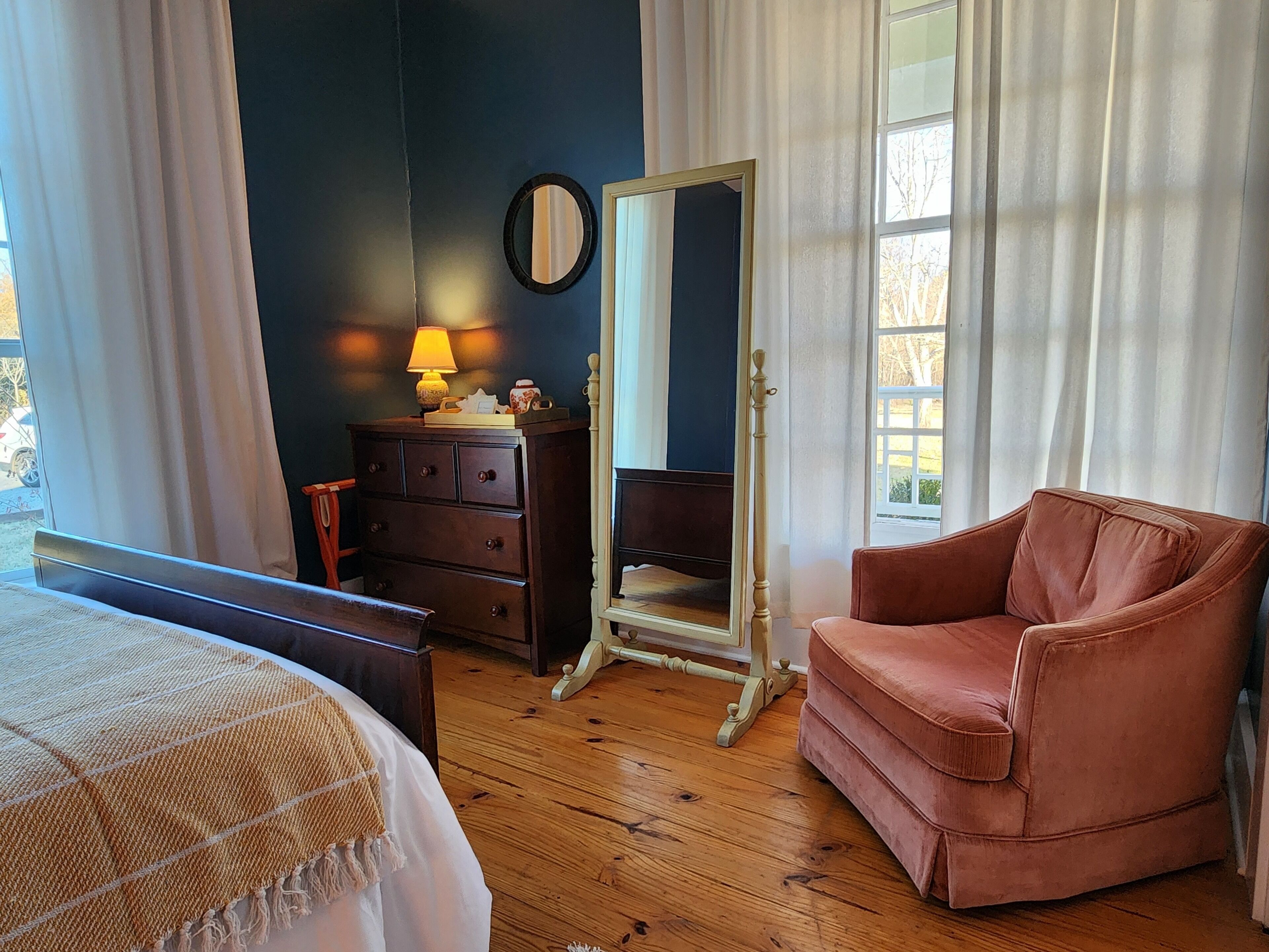A bedroom with a bed, a dresser, a mirror, a chair, and a window with curtains.