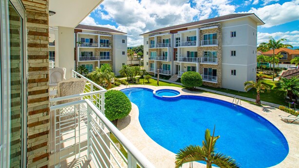 Um hotel moderno com piscina, várias varandas e um jardim bem cuidado.