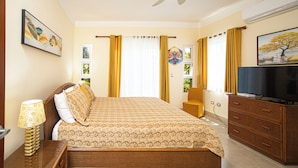 Quarto de hotel com cama, televisão, escrivaninha e ventilador de teto.