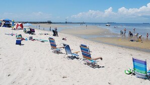 A beach with multiple colorful beach chairs and umbrellas, a pier in the background, and a calm sea.
