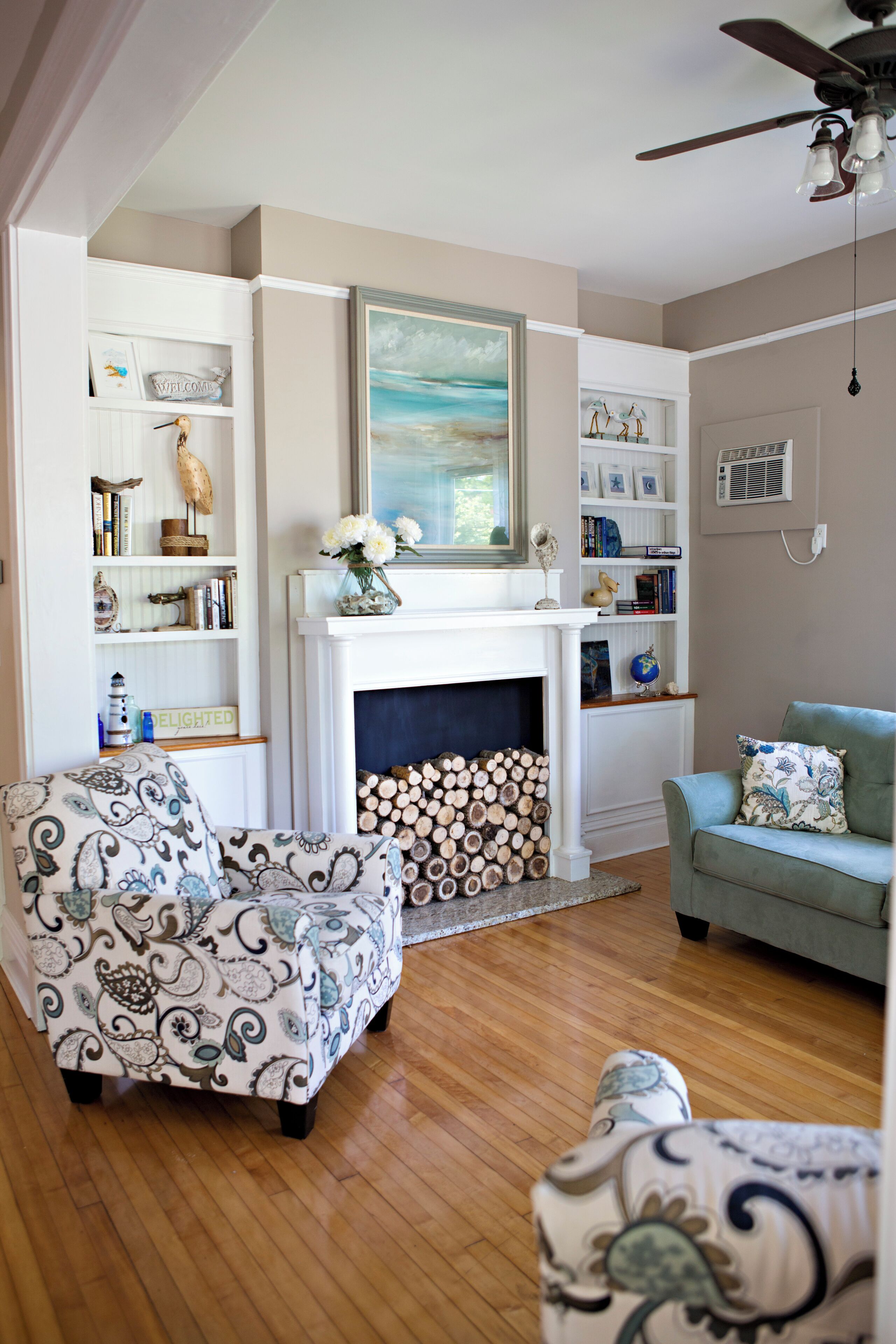 A living room with a fireplace, bookshelves, and two patterned armchairs.