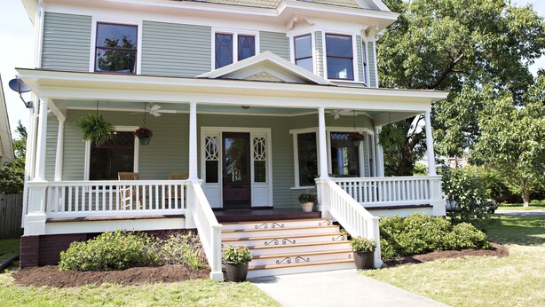 A two-story house with a front porch, a covered entryway, and a small front yard with plants.