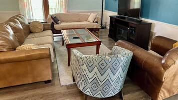 A living room with a sofa, armchair, coffee table, and a television.