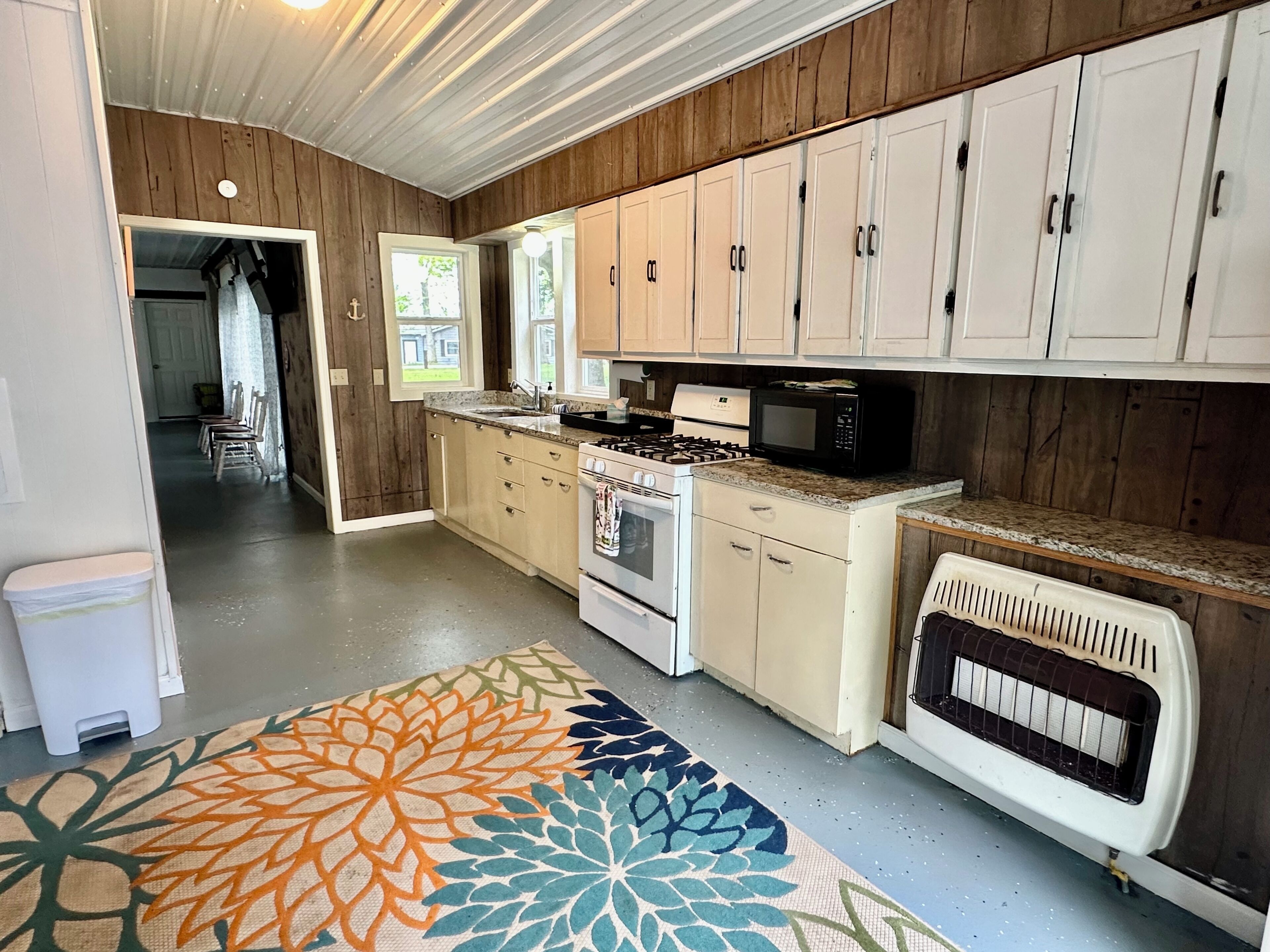 A kitchen with wooden cabinets, a stove, a microwave, and a patterned rug.