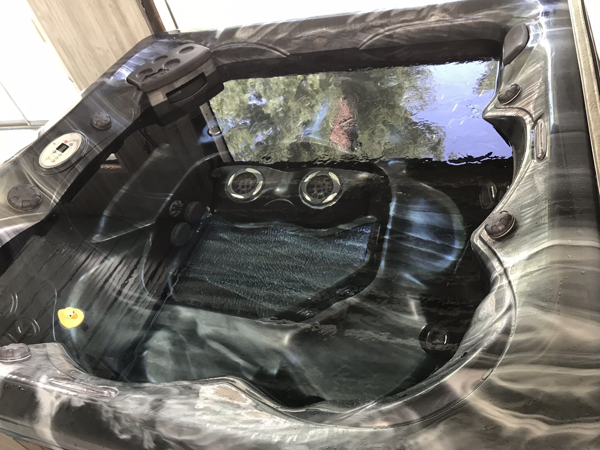 Un jacuzzi con panel de control, tapa de desagüe y vista a los árboles por la ventana.
