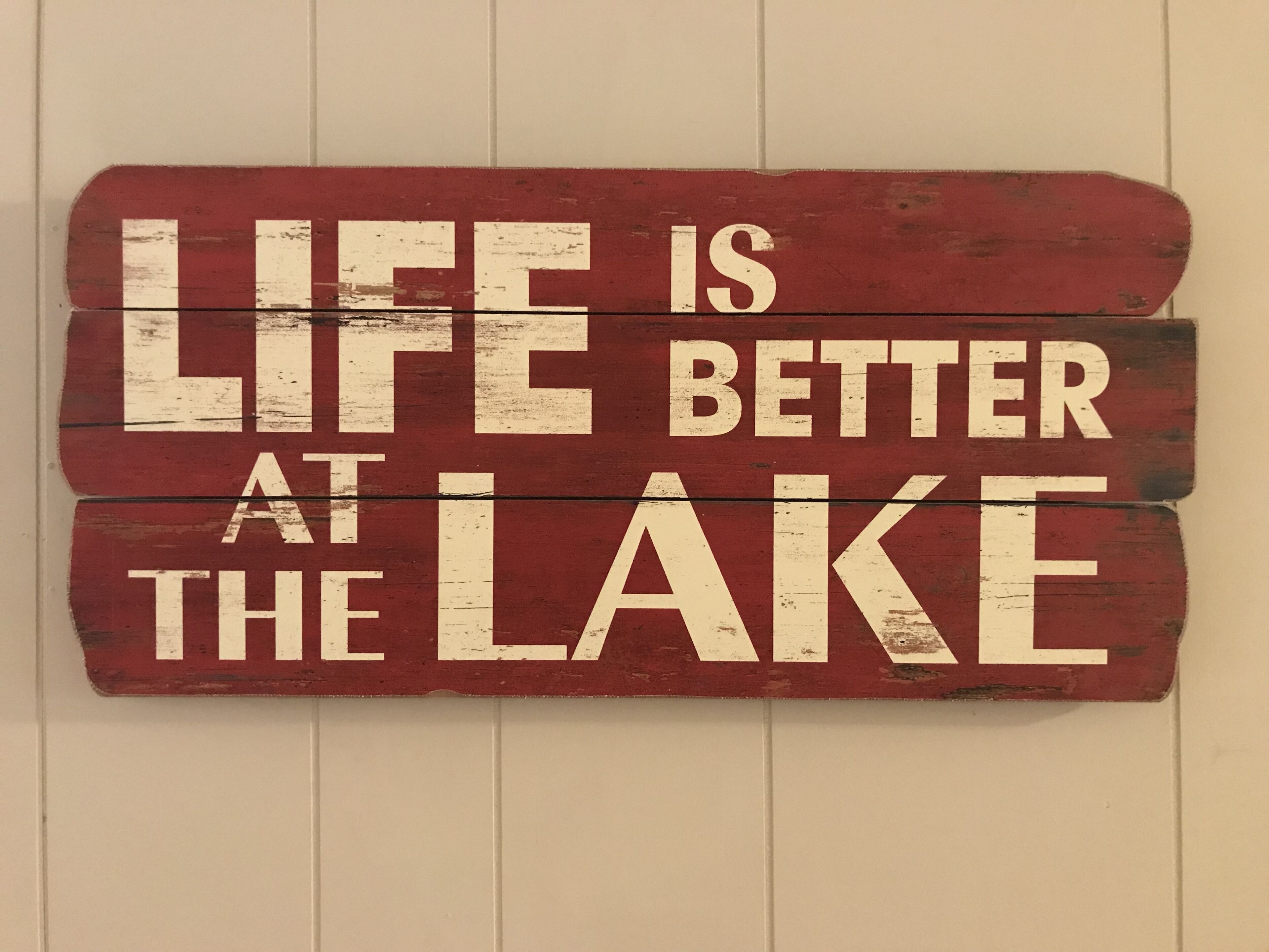 A wooden sign with the text "LIFE IS BETTER AT THE LAKE" mounted on a wall.