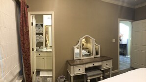 Un dormitorio con cama, cómoda con espejo, puerta que da a un baño y un pasillo.