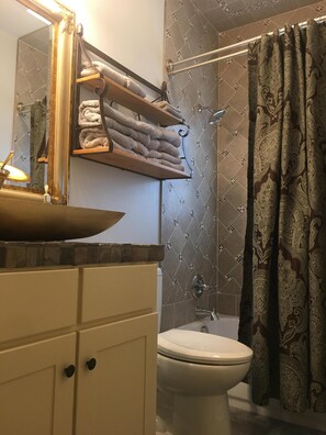 Ein Badezimmer mit einer weißen Toilette, einem Waschbecken mit Spiegel darüber, einem Handtuchhalter mit gefalteten Handtüchern und einer Duschvorhang mit Paisley-Muster.