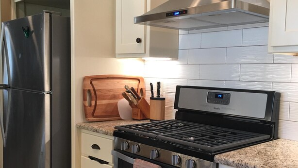 Una cocina moderna con electrodomésticos de acero inoxidable, una estufa a gas y armarios blancos.
