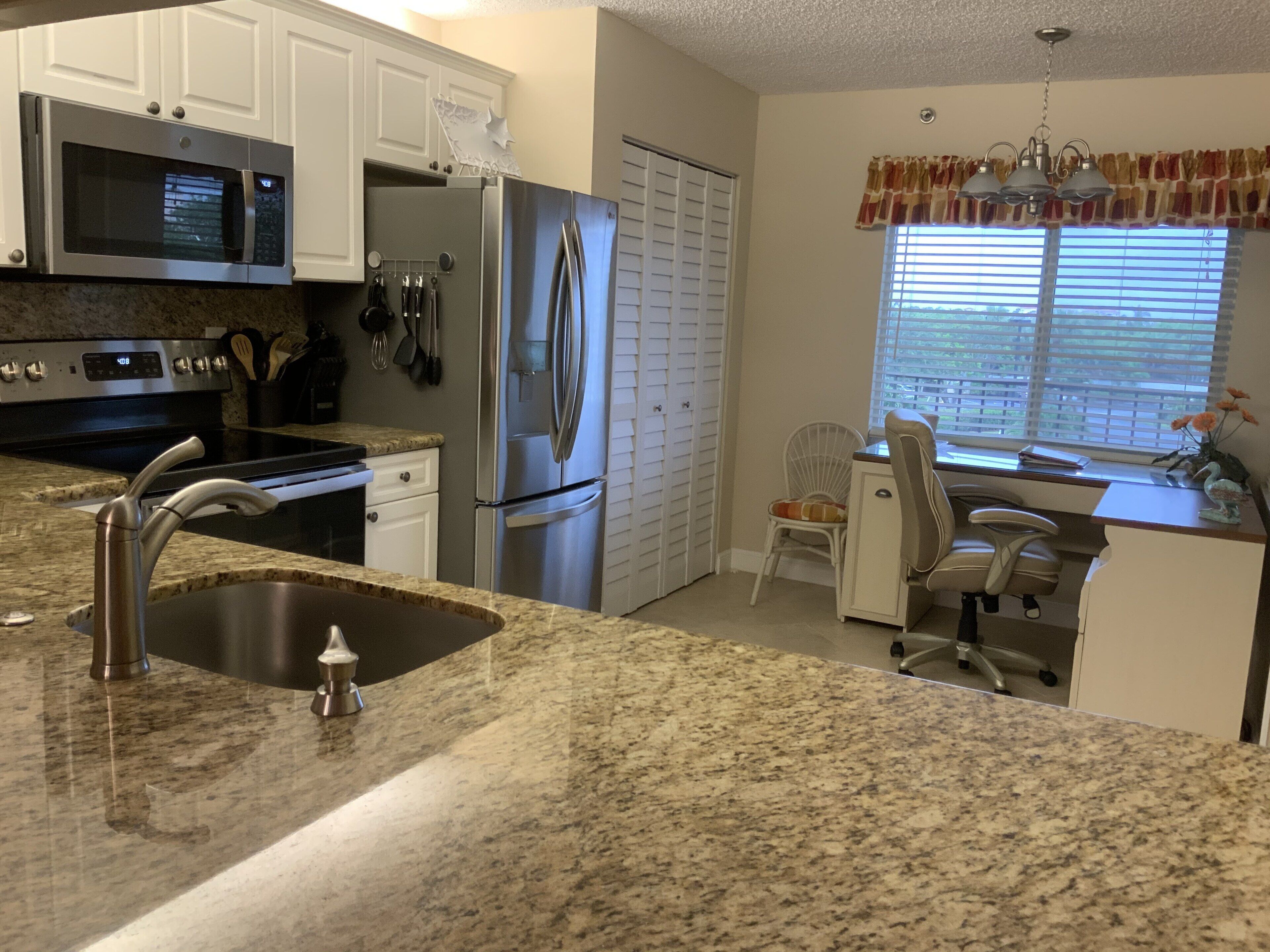 A kitchen with granite countertops, stainless steel appliances, white cabinets, and a window with blinds.